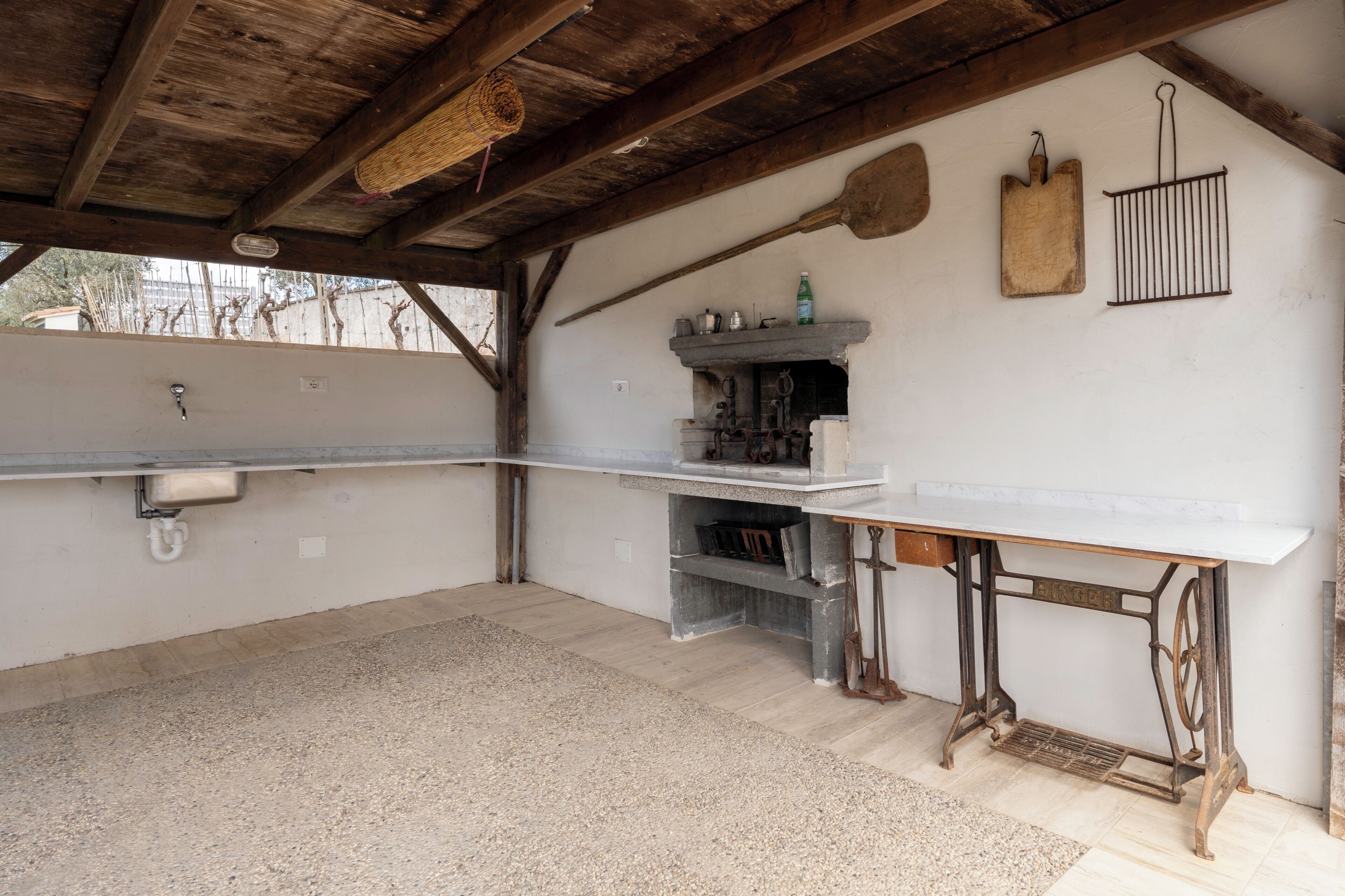 A rustic kitchen with a wooden ceiling, a sink, a shelf with kitchen utensils, and a hanging rack.