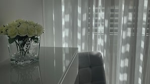 A modern room with a glass table, a vase with white flowers, and a grey upholstered chair. - Alissa Suite (Rome)