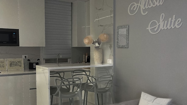 A modern kitchen with a marble countertop, a built-in microwave, and a bar area with stools. - Alissa Suite (Rome)