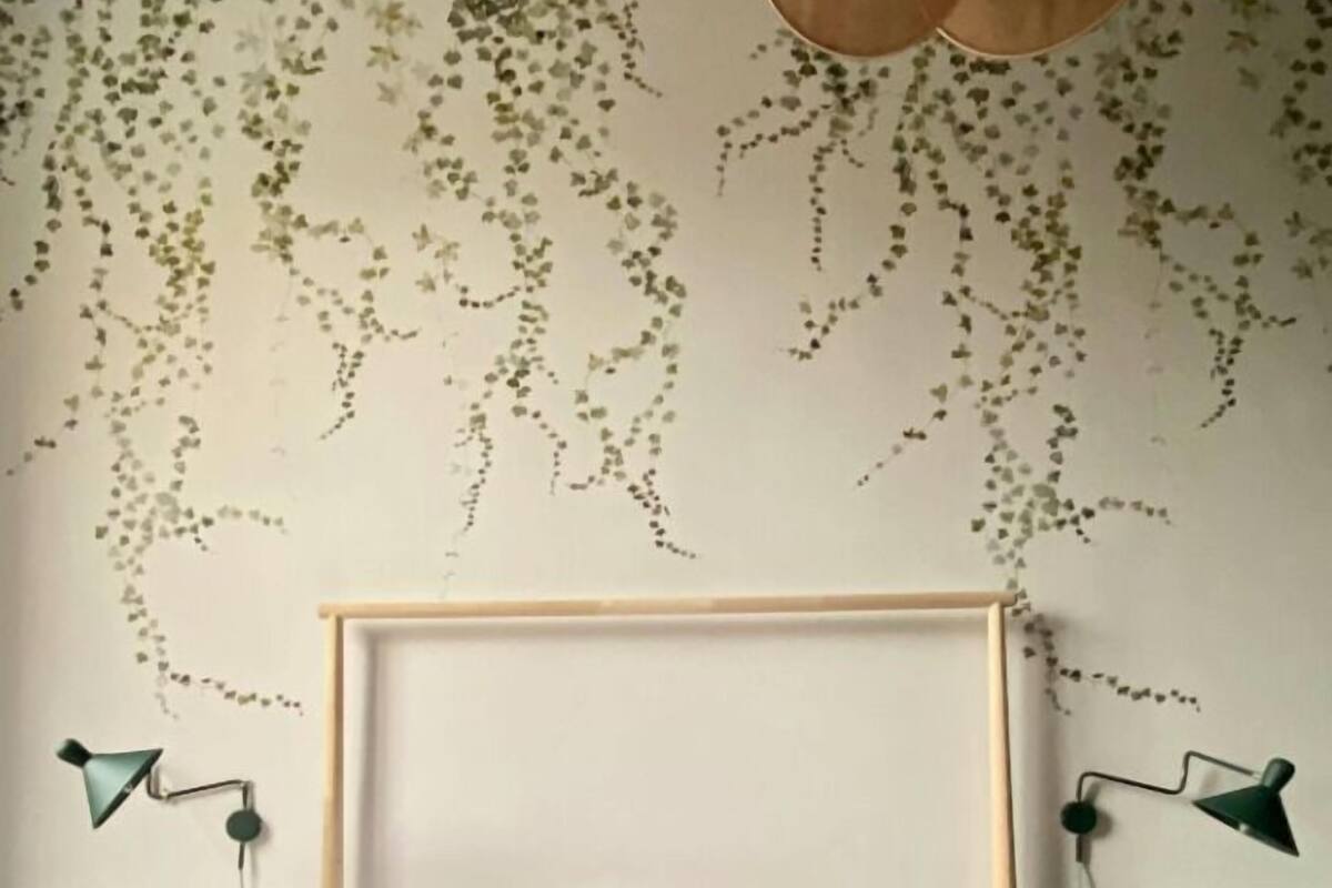 Ein Schlafzimmer mit einem Bett, zwei Nachttischen, einem Kopfteil und einer Wand mit hängenden Pflanzen.
