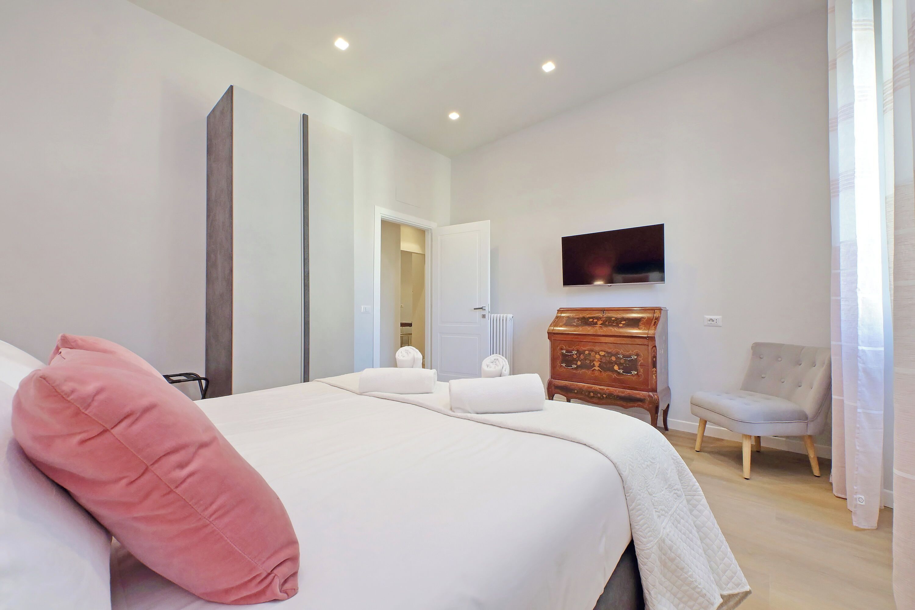 Une chambre à coucher moderne avec un grand lit, une commode en bois, un téléviseur et un fauteuil.