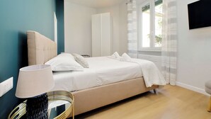 Un dormitorio con cama, mesita de noche, lámpara, espejo y ventana con cortinas.