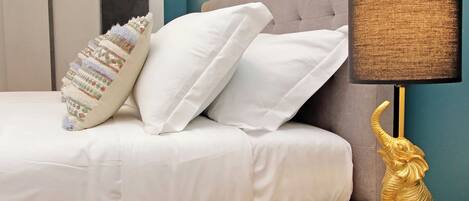 A bed with white and patterned pillows, a beige headboard, and a gold elephant lamp on a glass table.