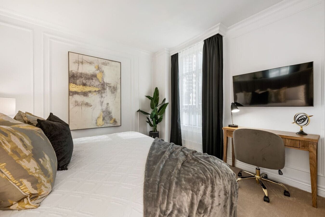 A hotel room with a large bed, a desk, a television, and a window with curtains.
