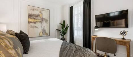 A hotel room with a large bed, a desk, a television, and a window with curtains.