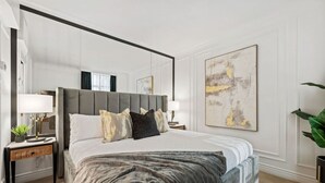 Une chambre à coucher moderne avec un grand lit, des tables de chevet, un miroir et un grand tableau abstrait accroché au mur.