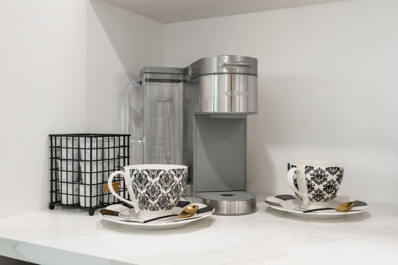 A kitchen area with a coffee maker, two cups, and a spice rack.