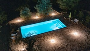 Ein rechteckiger Swimmingpool mit einer umlaufenden Steindeckplatte, ausgestattet mit Außenmöbeln und Beleuchtung.