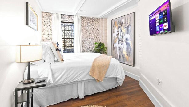 A bedroom with a bed, bedside table, lamp, and a TV displaying streaming services. - Comfortable Apartment - 5 mins from UAB & Hospitals (Birmingham)