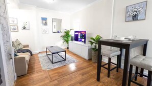 A modern living room with a sofa, a coffee table, a TV, and a dining area with a table and chairs. - Comfortable Apartment - 5 mins from UAB & Hospitals (Birmingham)