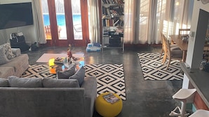 A living room with a sofa, coffee table, ottoman, and a bookshelf. - The Bakers Villa- Old Wharf Limited (Treasure Beach)