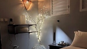 A bedroom with a bed, a wall-mounted shelf, a decorative branch with lights, a patterned rug, and a bedside table with a lamp. - The Bakers Villa- Old Wharf Limited (Treasure Beach)
