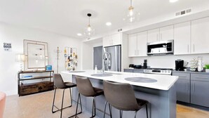 Una cocina moderna con una isla central, taburetes de bar, electrodomésticos de acero inoxidable y un salpicadero blanco.
