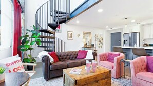 Una sala de estar moderna con un sofá de cuero marrón, un sillón rosa, una mesa de centro de madera y una escalera en espiral.