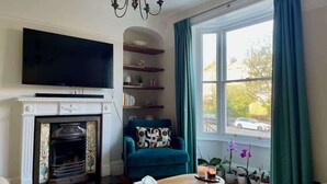 A living room with a fireplace, television, teal armchair, and a window with curtains.