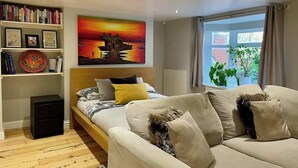 A modern living room with a bed, a sofa, a bookshelf, and a large painting.