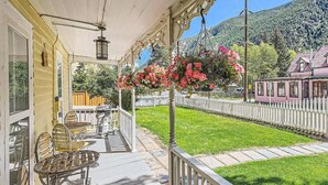 Een overdekt terras met buitenmeubilair, een wit hek en uitzicht op een berg.