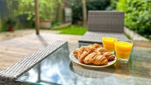 A glass table with croissants and orange juice, set outdoors with a wicker chair and a view of greenery. - Modern 3 Bed Home - Pets Welcome + FREE Parking (Canterbury)