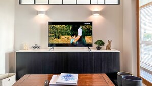 A living room with a flat-screen TV mounted on a wall, a wooden dining table, and a cabinet below. - Modern 3 Bed Home - Pets Welcome + FREE Parking (Canterbury)