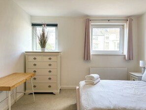 Une chambre à coucher avec un lit, une commode, une fenêtre avec des rideaux et un radiateur.