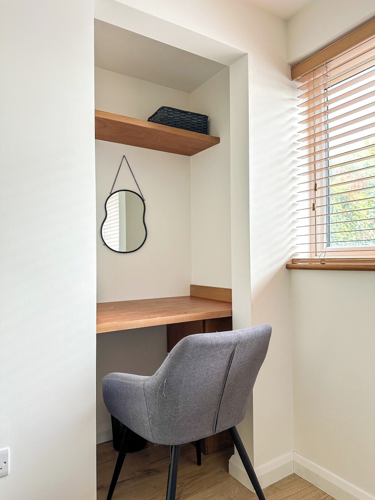 A compact room with a desk, a chair, a mirror, and a window with blinds.