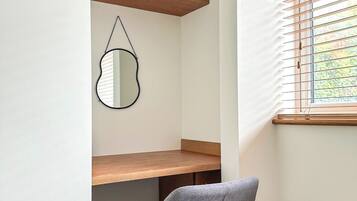 A compact room with a desk, a chair, a mirror, and a window with blinds.