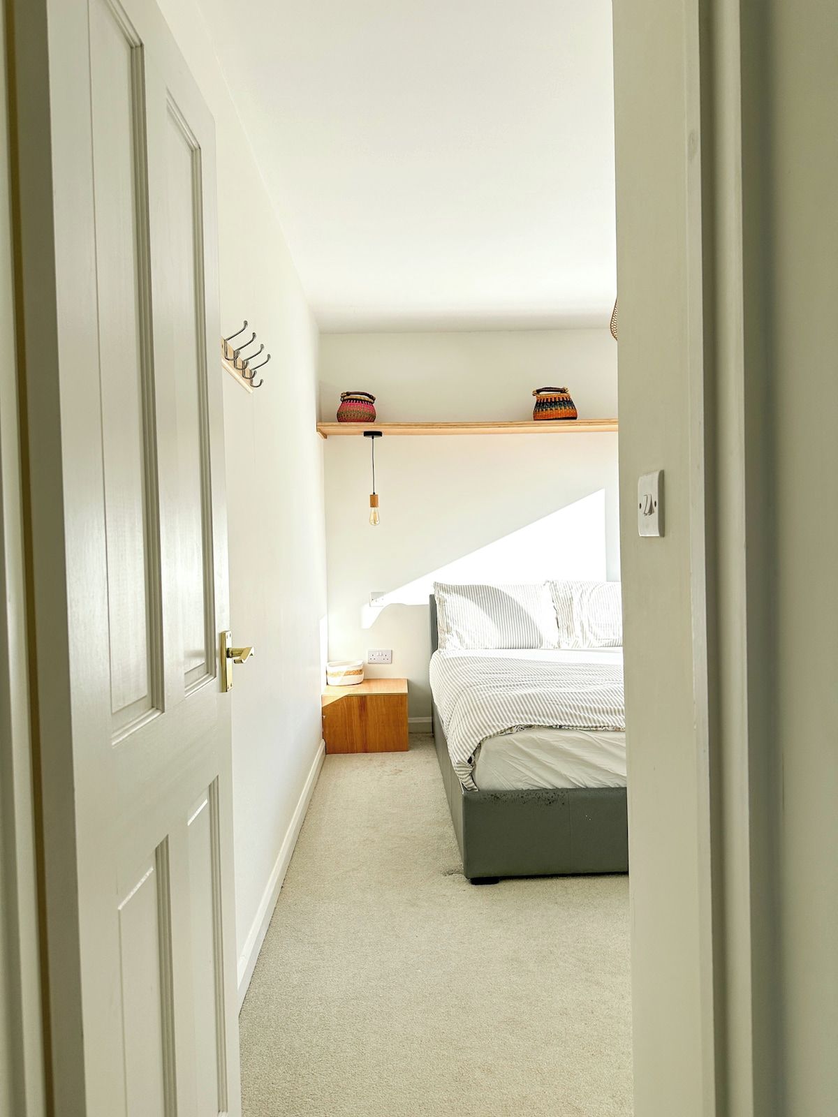 A bedroom with a bed, a nightstand, a shelf with decorative items, and a hanging light fixture.
