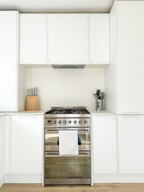 Een keuken met witte kastjes, een roestvrijstalen fornuis en een houten snijplank.