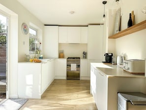 A compact kitchen with white cabinets, a stove, a coffee maker, and a toaster.