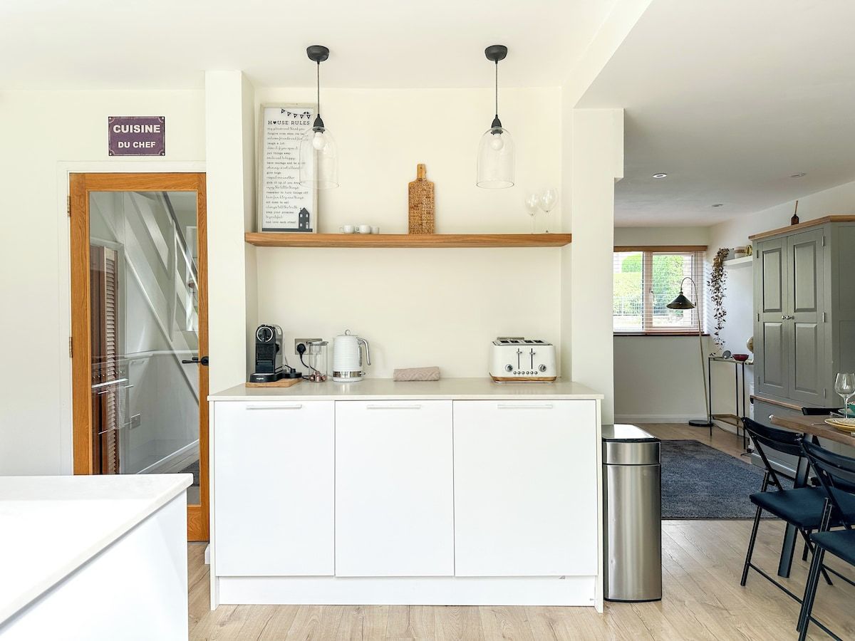 A modern kitchen with white cabinetry, a coffee machine, a toaster, and a hanging light fixture.