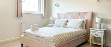 Un dormitorio con cama, mesitas de noche, una ventana con cortinas y una lámpara de pared.