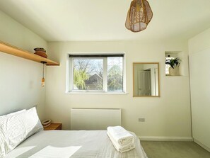 A bedroom with a bed, a window, a bedside table, a mirror, and a hanging light fixture.