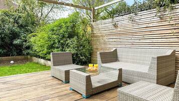 Un patio al aire libre con mobiliario de mimbre, incluyendo un sofá y dos sillones, y una mesa de centro de vidrio.