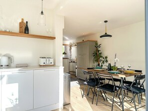 Een moderne keuken met een eethoek, met een witte koelkast, een broodrooster en een houten eettafel met stoelen.