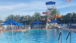 A swimming pool with blue umbrellas, a lifeguard tower, and a no-jumping sign. - Family fun amenities for all ages!Two bedroom ,sleeps 6, pet friendly ,relaxing. (Sarasota)