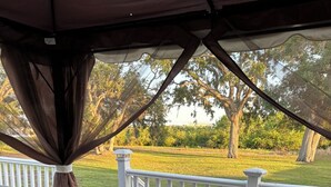 A covered outdoor seating area with teal cushions and wicker chairs, overlooking a grassy field and trees. - Family fun amenities for all ages!Two bedroom ,sleeps 6, pet friendly ,relaxing. (Sarasota)