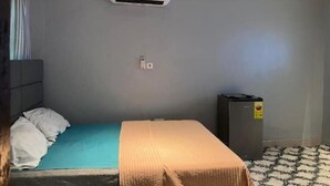 Ein Hotelzimmer mit Bett, Kissen, Decke, Klimaanlage, Mülleimer und einem gemusterten Teppich.
