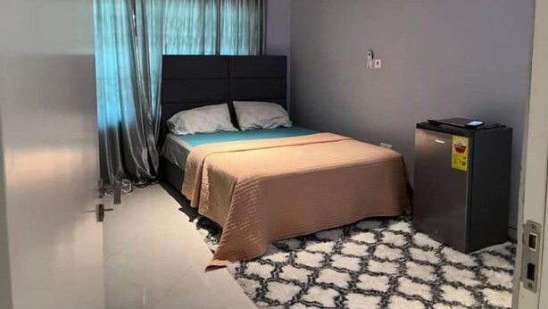 Ein kleines, ordentlich eingerichtetes Schlafzimmer mit Bett, einem kleinen Schrank und einer Klimaanlage an der Wand.