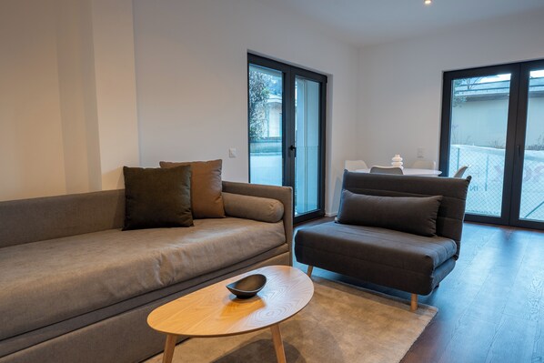 A modern living room with a grey sofa, a smaller grey armchair, and a round wooden coffee table. - Modern Concept Suite Crocetta 3 in Lugano (Lugano)