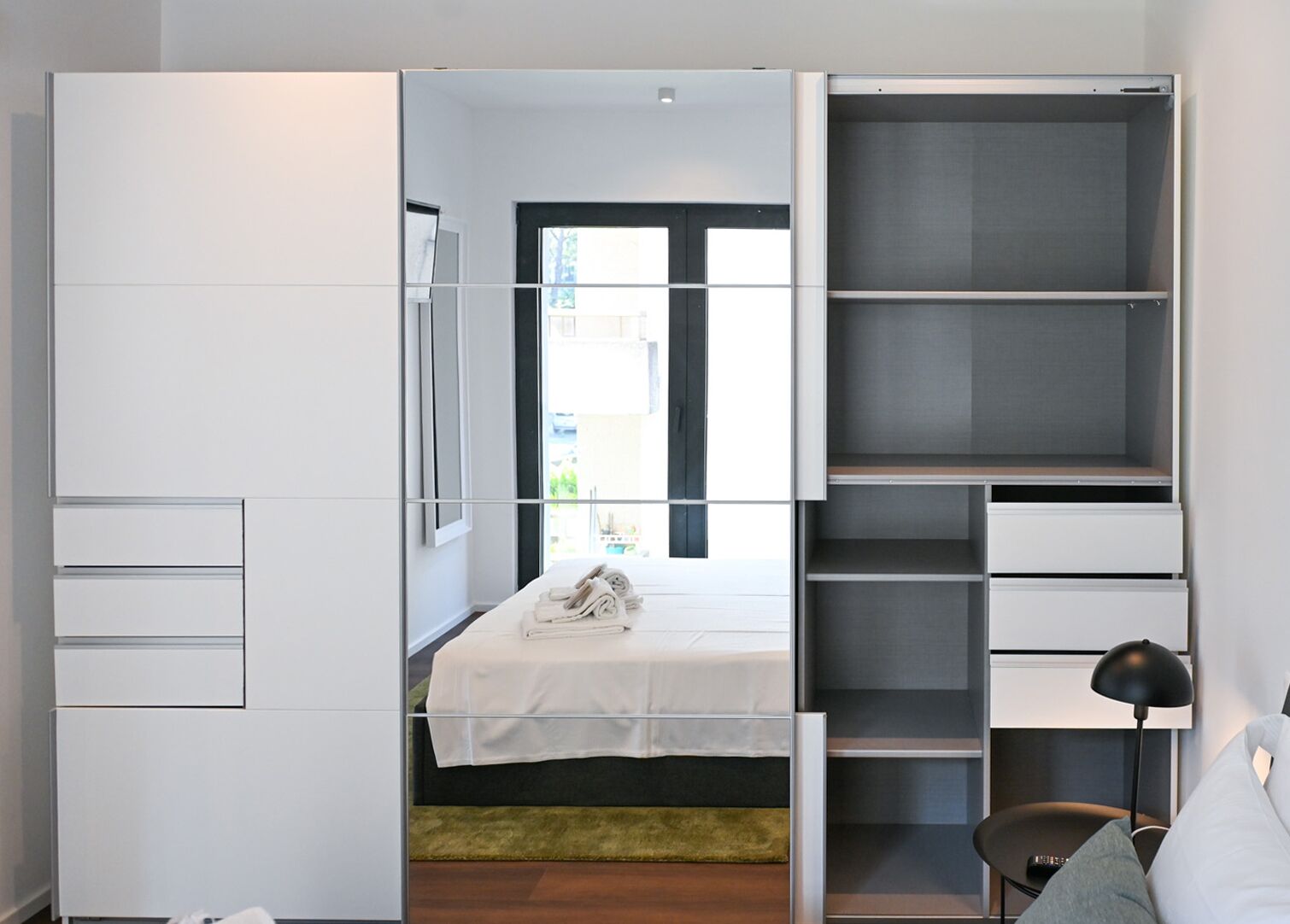 A modern bedroom with a bed, built-in wardrobe, and a view through a window.