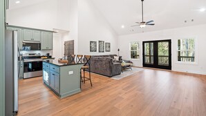 A spacious kitchen with modern appliances, a dining area with a gray sofa, and large windows offering natural light.