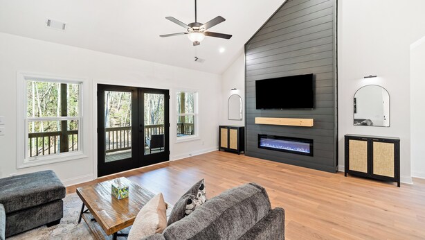 A modern living room with a flat-screen TV, a fireplace, and a ceiling fan.