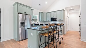 A modern kitchen with light green cabinets, stainless steel appliances, and a central island with bar stools.