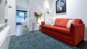 Ein modernes Wohnzimmer mit einem roten Sofa, einem schwarz-weißen Teppich, einer Blumenvase und einem gerahmten Bild an der Wand.