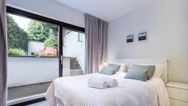 Ein Schlafzimmer mit einem großen Bett, einer Schiebetür zum Balkon und einem kleinen Fenster mit zwei Bildern an der Wand.