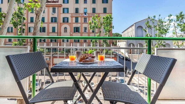 Un balcon avec deux chaises, une table et un plateau de petit-déjeuner comprenant des croissants et du jus d’orange.