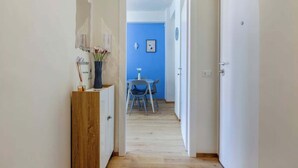 Un couloir mène à une salle à manger avec un mur bleu et une table entourée de chaises.