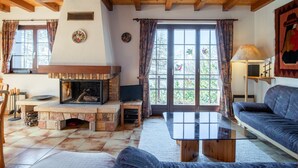 Una sala de estar acogedora con chimenea de piedra, un sofá, una mesa de centro y un ventanal con cortinas.