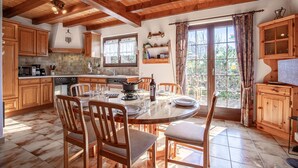 Una cocina de madera con una mesa de comedor para cuatro personas, armarios de madera y una ventana con cortinas.