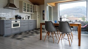 A modern kitchen with grey cabinets, a wooden ceiling, and a large window overlooking a mountainous landscape. - STUDIO.LOFT.MOUNTAINS (Collombey-Muraz)